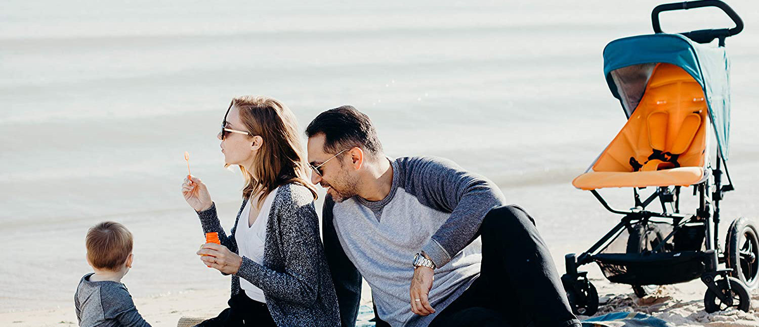 Mum, dad and toddler having picnic on beach, sitting next to pushchair