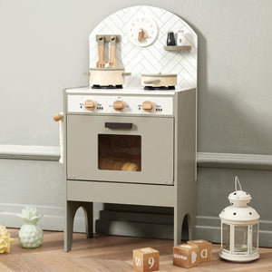 Children's play kitchen set with toy stove, oven, and accessories on a wooden floor.