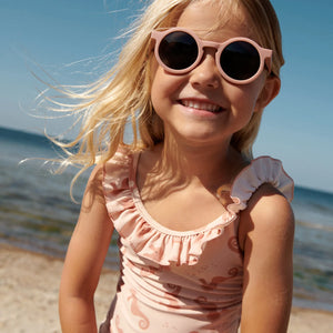 A girl is smiling, wearing a swimsuit on the beach in summer.
