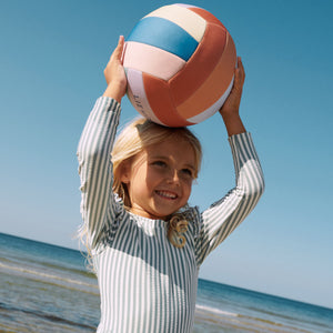 A girl is playing in the beach with liewood volley ball.