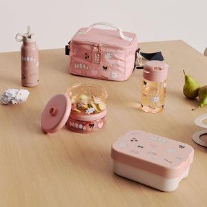 A lifestyle photo on a light wooden table showing the mood pale tuscany insulated lunch bag, a matching pink water bottle, and an open pink lunchbox containing snacks.