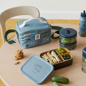 A lifestyle photo on a wooden surface showing the open play dusty peppermint lunch bag, a matching green snack container, and an open lunchbox filled with food.