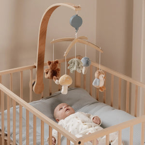 A baby is watching or playing with the wooden musical cot mobile.
