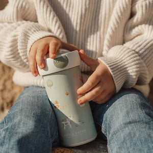 Close-up of a child wearing a white sweater and blue jeans holding the Little Farm school beaker in their lap.