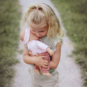 A young child outdoors, lovingly cradling the Little Dutch Baby Lily doll in her arms.