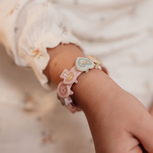 A close-up of a child's wrist wearing a pastel silicone bracelet with cute character charms, including a moon and a flower.