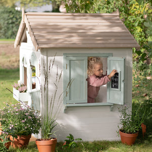 Little dutch wooend playhouse sitting beautifully on a green lawn, surrounded by garden plants and sunshine.