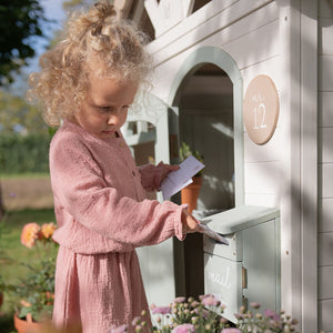 Child in a pink dress interacting with a mailbox attached to a playhouse.