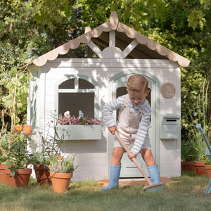 A child is pretend working in the garden in front of the little ducth wooden garden playhouse.