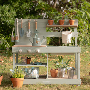 Little Dutch wooden mud kitchen fully styled with potted plants and garden tools outdoors on a sunny lawn.