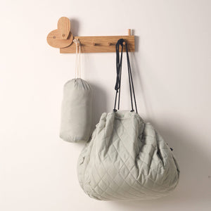 ight grey storage bag and its matching small cylindrical travel pouch hanging together on a wooden peg rail.