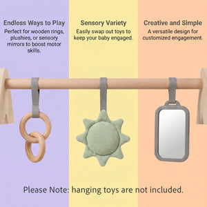 Three baby sensory toys hanging from a wooden baby gym against a tri-color pastel background: a wooden ring and loop, a mint green sun-shaped plush, and a rectangular mirror with a gray frame. Text describes the toys' benefits, and a note says hanging toys are not included.