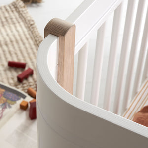 Minimalist wooden cot bed with soft, curved details.