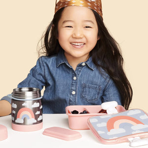 A girl is sitting in front of Skip Hop lunch box with food