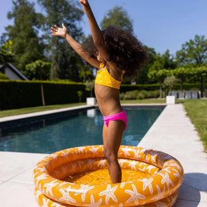 A girl is playing in the inlfatable baby pool near the swimming pool.
