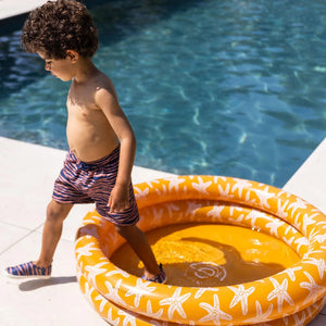 A boy is playing in the inflatable baby pool.