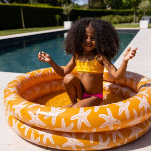 A girl is having fun in the sun in the baby pool, near the swimming pool.
