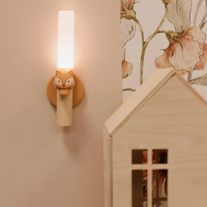 Wall-mounted light fixture with fox design on a wall with floral wallpaper.
