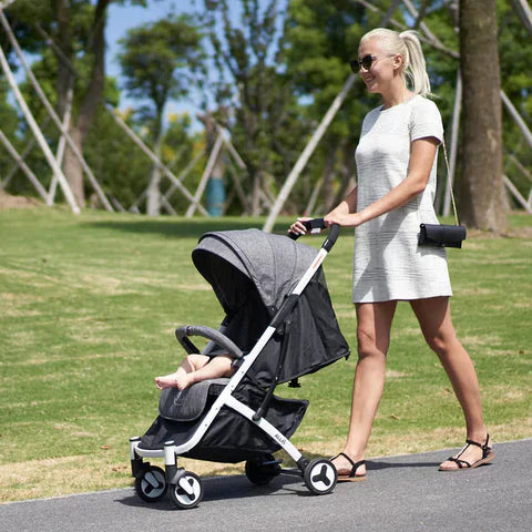 A mum is moving a baby in a black Pushchair.