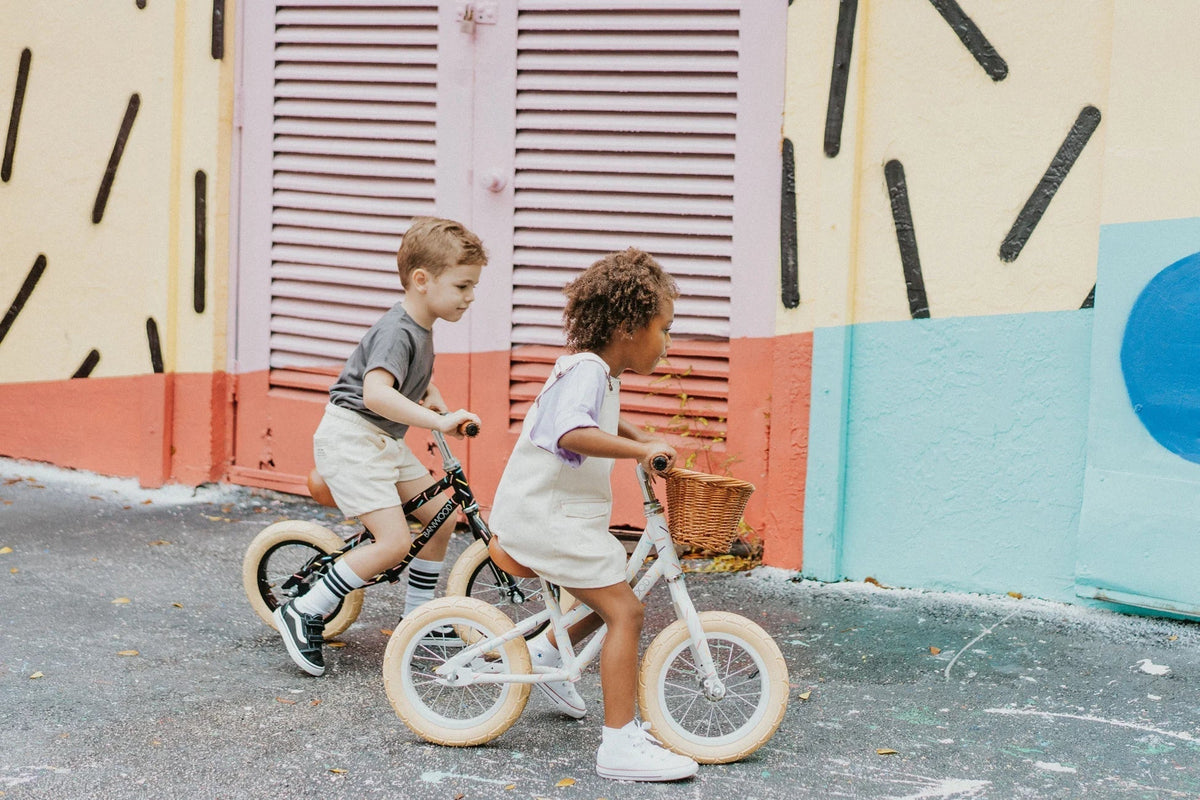 Two young children playing outdoors with a Banwood balance bike, enjoying a sunny day while building balance and coordination skills.