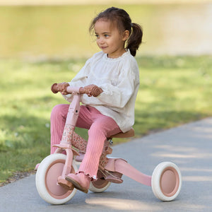 A young girl confidently riding the Little Dutch 4-in-1 Tricycle in pink outdoors on a paved path, showcasing the classic tricycle mode with independent pedalling.