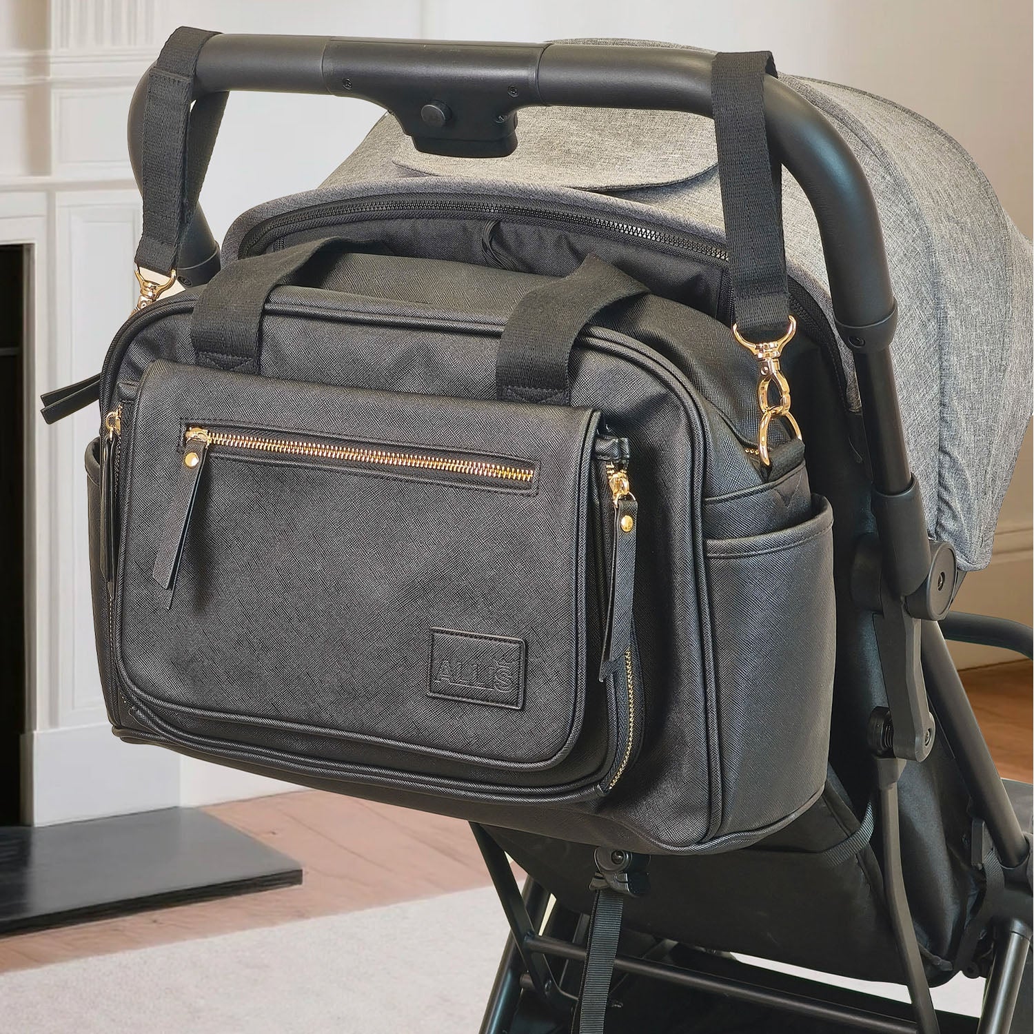 Black diaper bag attached to a flick stroller with a white wall background