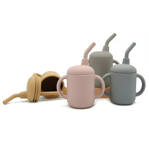 Pink, blue, and yellow silicone toddler sippy cups standing next to a beige canvas pouch.