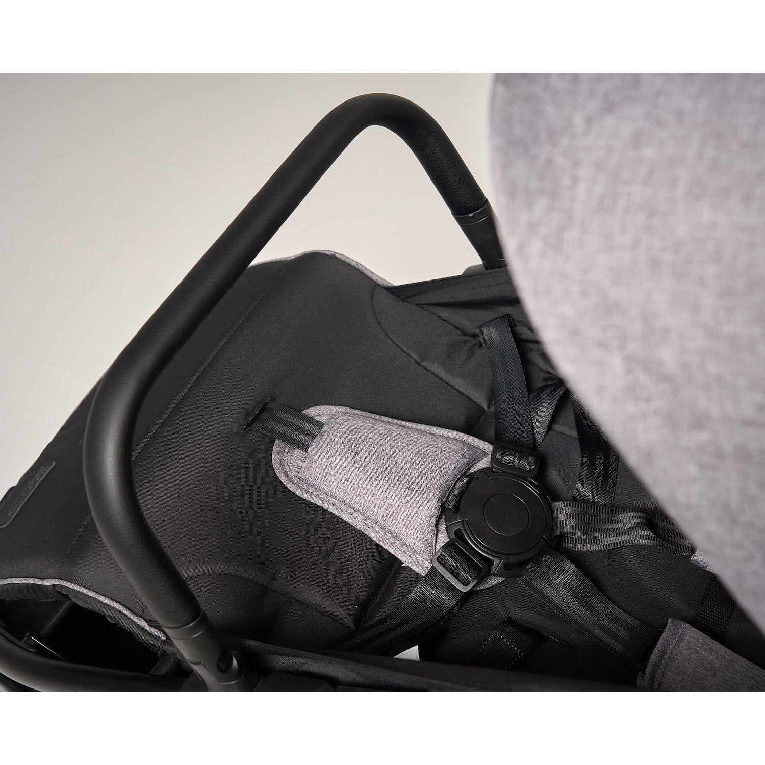 Close-up of a flick stroller seat with a grey cover and black straps on a neutral background