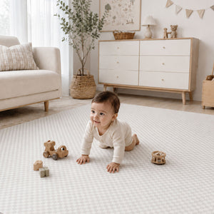 A baby crawling on a light beige and white patterned play mat in a bright, modern nursery. The baby is wearing a cream long-sleeve bodysuit and looking to the side.