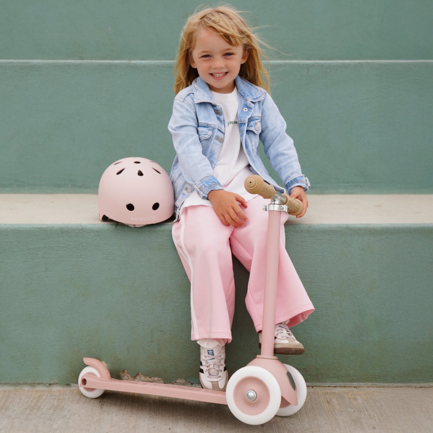 A girl is seating with banwood eco scooter with helmet.