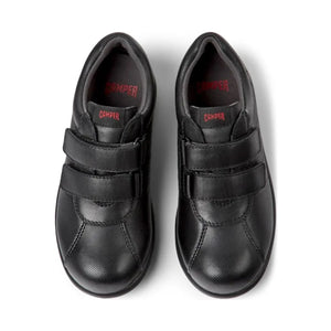 Top view of Camper Pelotas black leather shoes for kids, highlighting the wide, comfortable fit and the cushioned EVA insole. The shoes have Camper branding on the inner lining and feature double hook-and-loop straps for secure closure.