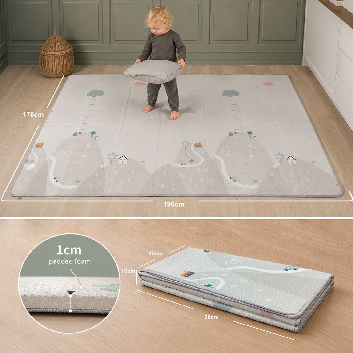 A large rectangular children's play mat with a light gray and white mountain-and-river landscape print is shown in a room, with a child standing on it and holding a pillow. White measurement lines and text indicate dimensions of the mat.