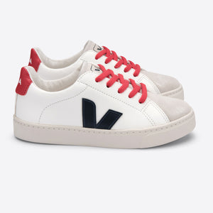 A pair of white and navy kids' sneakers with red laces and a distinctive 'V' logo on the side, featuring a chrome-free leather upper and Amazonian rubber sole.