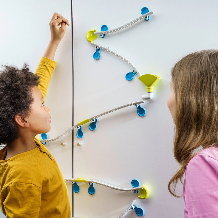 Kids building a Gecko Run marble track on a wall, showing the flexible tracks and curves.