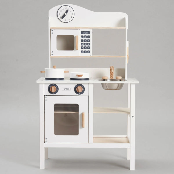 A close-up photo of a white wooden play kitchen for kids. The kitchen has a microwave, a stove with two burners, a sink, and a clock. There are also cabinets and shelves for storage.