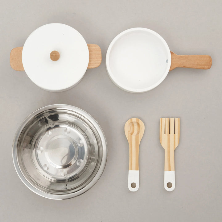 A set of stainless steel pots and pans, a stainless steel bowl, and wooden utensils arranged on a wooden table.