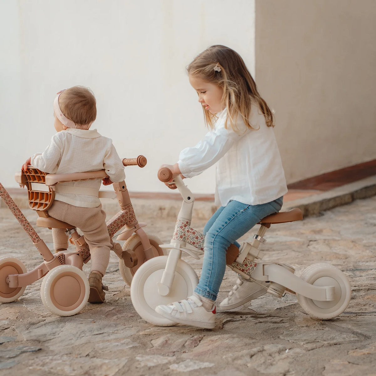 Two young children playing indoors with the Little Dutch 4-in-1 Tricycle in pink, demonstrating the classic independent pedalling mode.