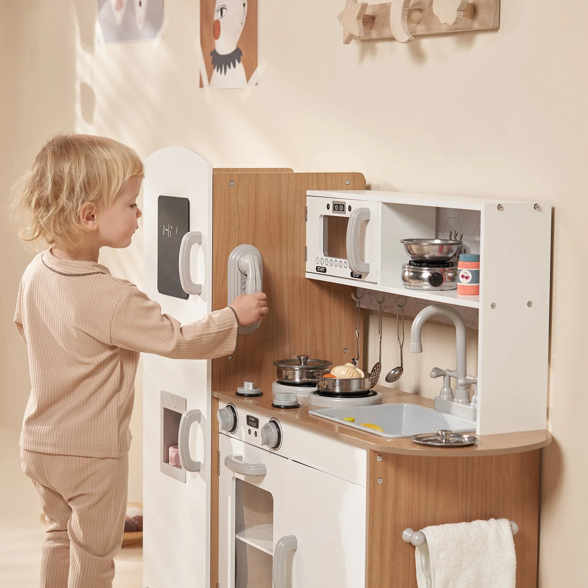 A young child standing up and interacting with telephone section of the Kidoz white wooden play kitchen.