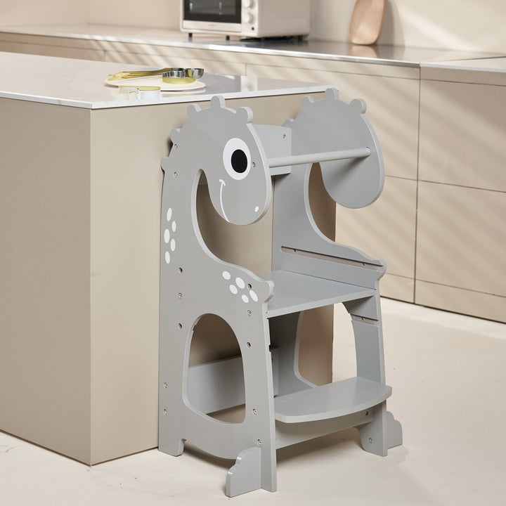 A sturdy wooden kitchen helper tower in the shape of a friendly baby dinosaur,, with three adjustable levels, safety rails, and a non-slip mat. Perfect for helping little ones reach countertops and participate in kitchen activities safely.