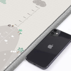 Close-up comparing the 1-centimetre thickness of the cushioned baby play mat to the edge of a standard black smartphone.