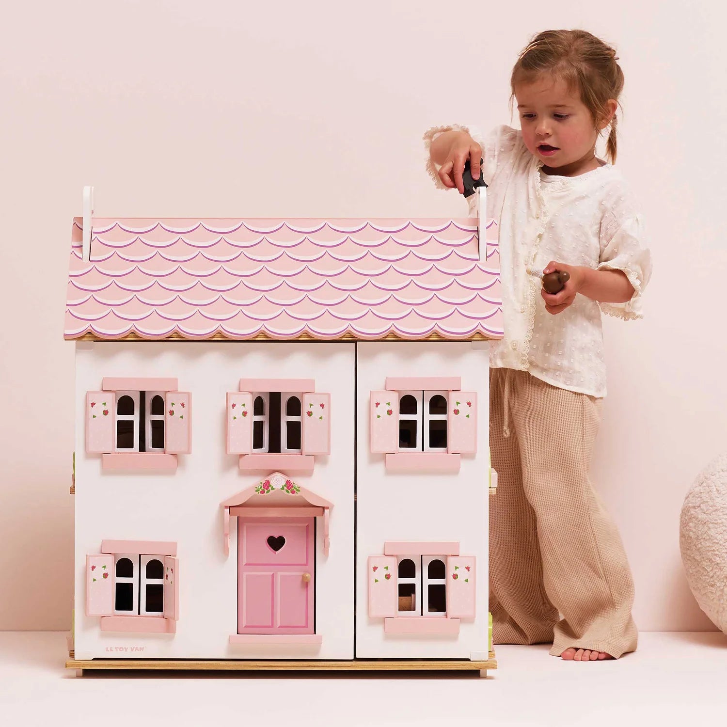 A little girl is playing with the le toy van dolls house in her playroom.