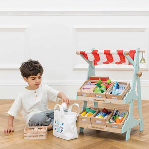 A boy is playing with the wooden market stall.