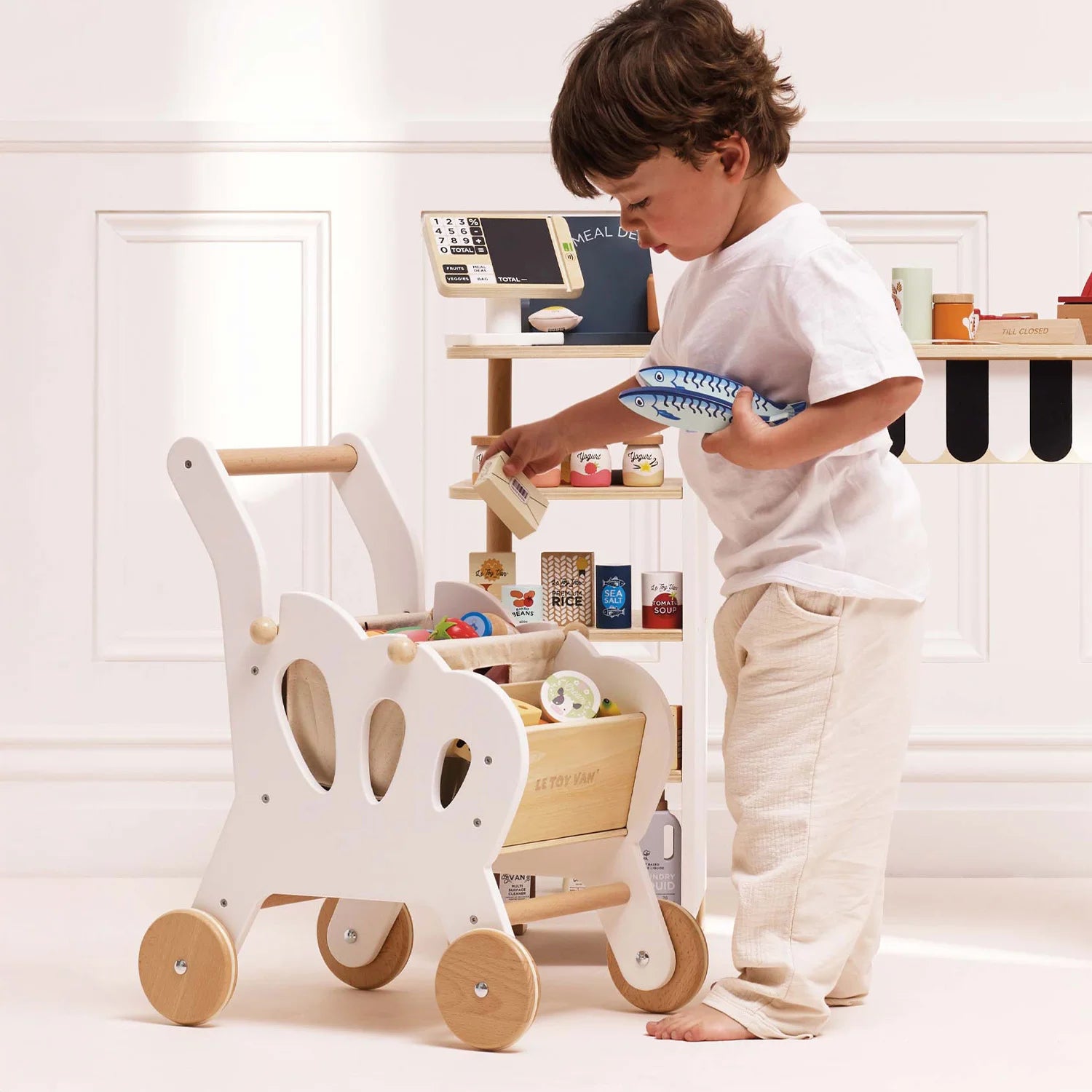 A toddler is playing with the Le Toy Van wooden trolley.
