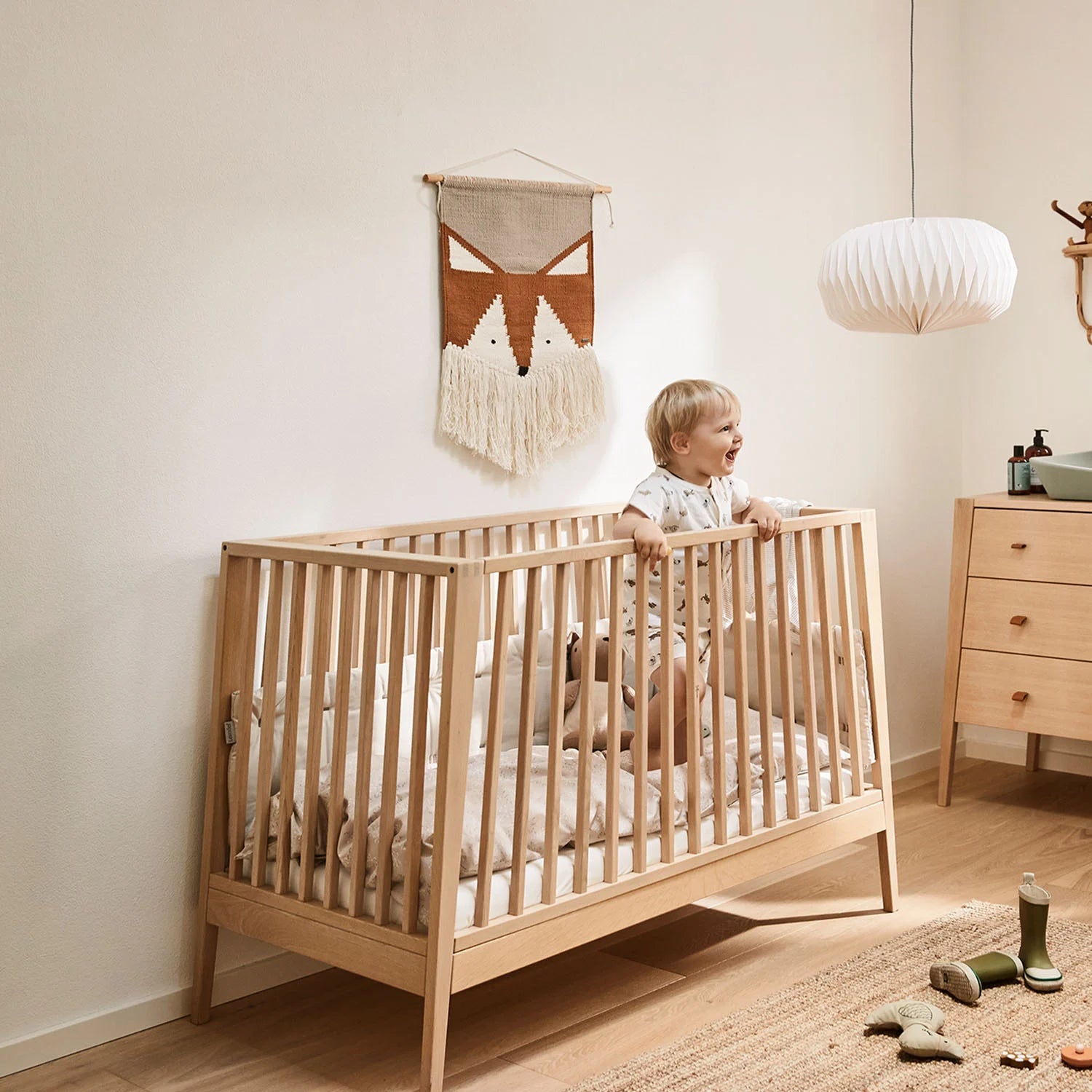 A toddler is trying to stand inside the baby cot.