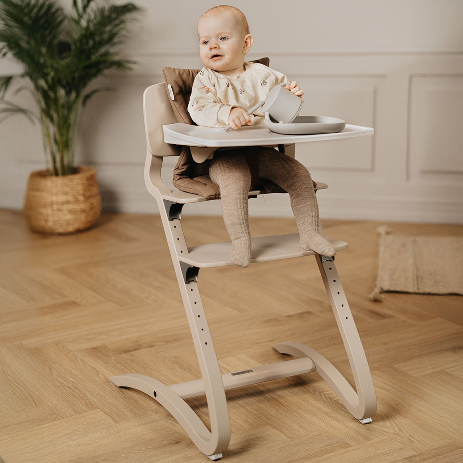 A Leander Louie highchair configured for a baby, featuring the safety bar, high backrest support, and an attachable tray for early weaning and first meals.