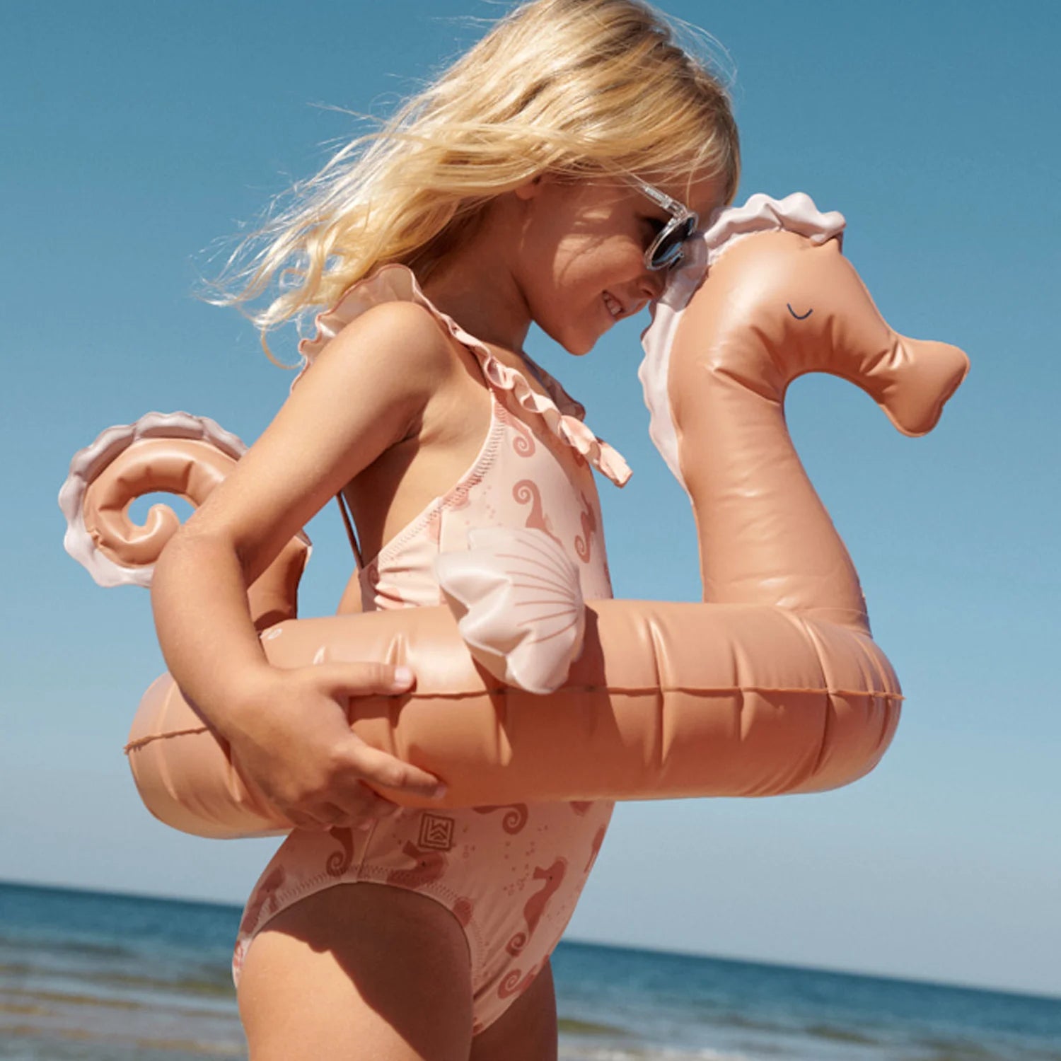 A girl is wearing a Liewood UV swimsuit on the beach.