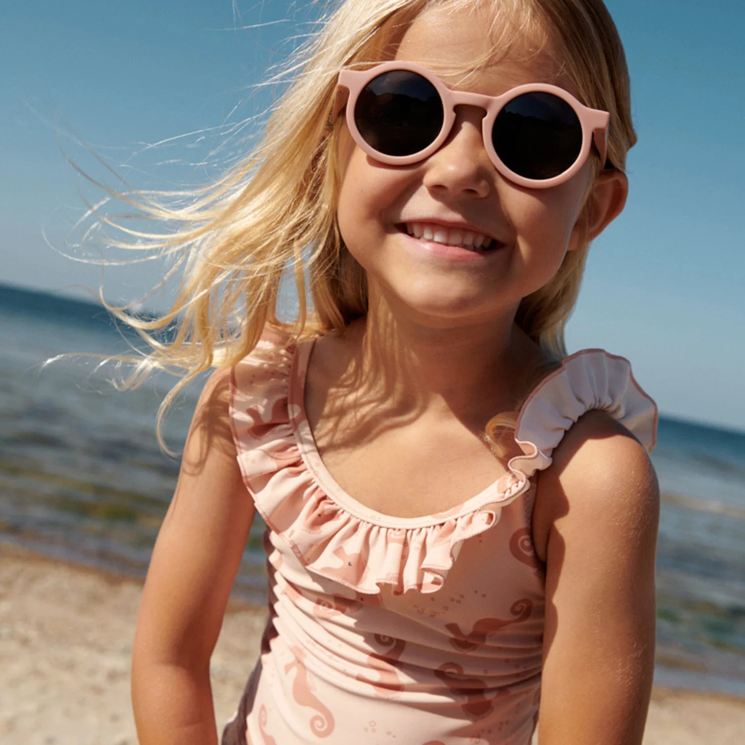 A girl is smiling, wearing a swimsuit on the beach in summer.