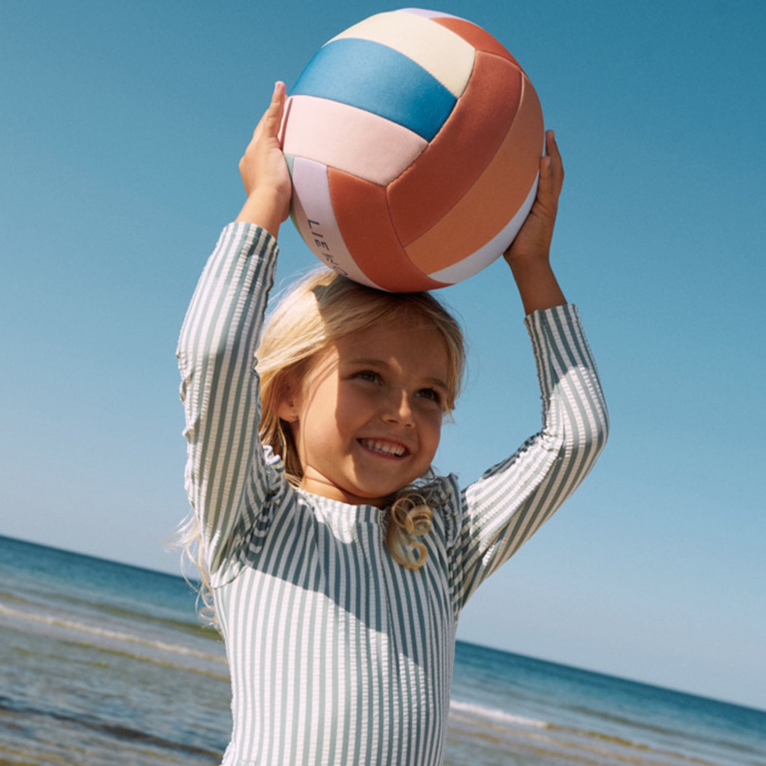 A girl is playing in the beach with liewood volley ball.