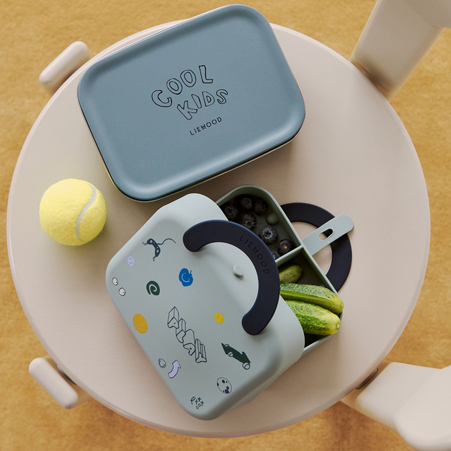Overhead view of a dusty peppermint Liewood Elara lunchbox packed with snacks on a kids' table next to a matching thermos lid.