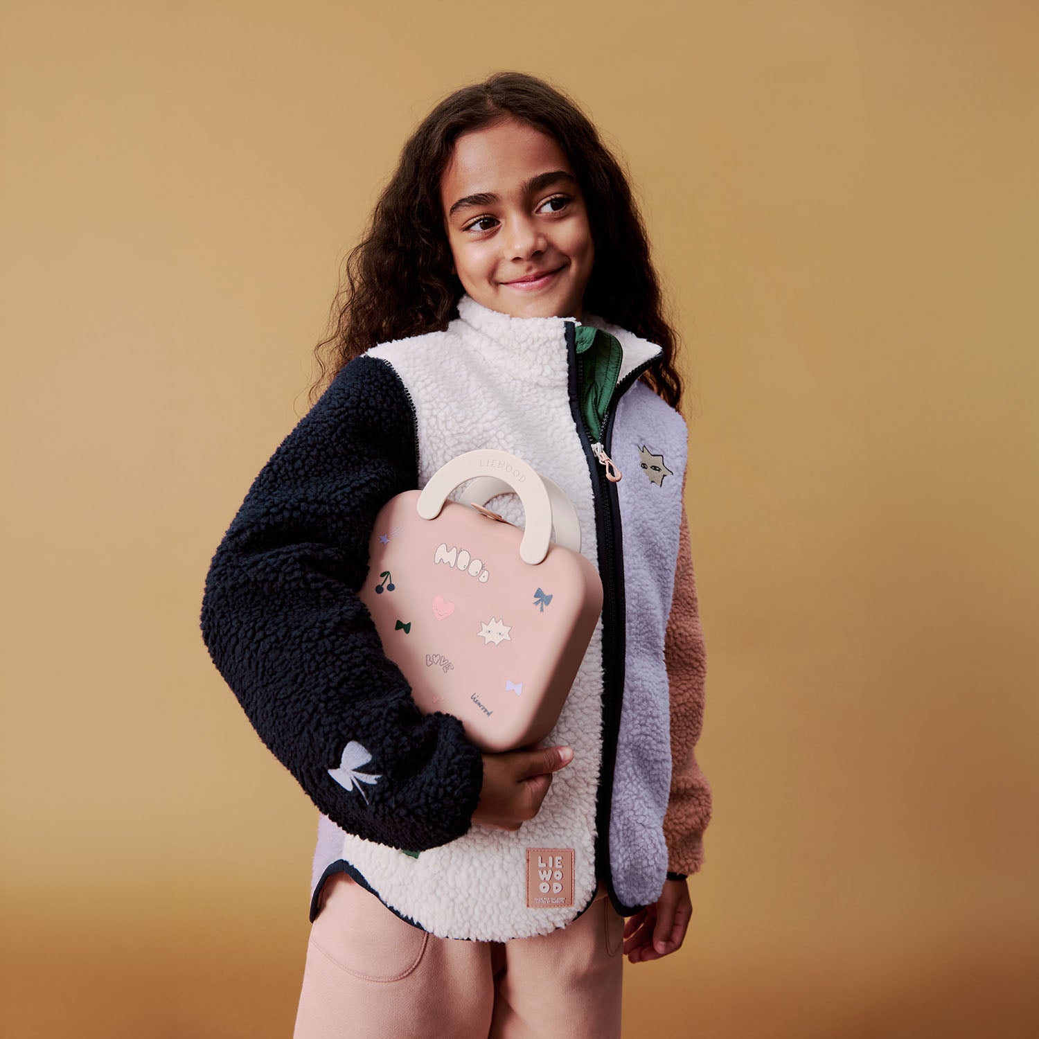 A young girl smiling and holding a mood pale tuscany Liewood Elara silicone lunchbox like a small handbag.